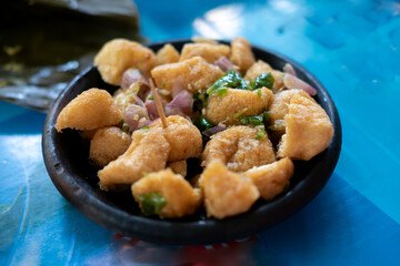 a serving of Tahu Gejrot, a popular Indonesian street food,  the fried tofu pieces mixed with a dark, watery sauce, slices of shallots, and green chili peppers in a dark bowl