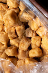 a close-up of golden-brown, deep-fried tofu cubes, likely Tau Pok, in a clear plastic bag.