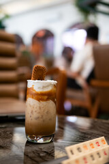 a layered iced coffee drink, likely a spiced cookie latte, served in a tall glass. It features layers of coffee, milk, and whipped topping, garnished with a spiced cookie.