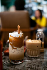 a layered iced coffee drink, likely a spiced cookie latte, served in a tall glass. It features layers of coffee, milk, and whipped topping, garnished with a spiced cookie.