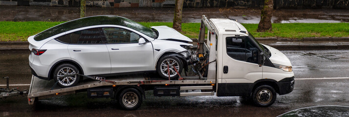 Tow truck with a broken car on road. Tow truck transporting a white car on the highway.