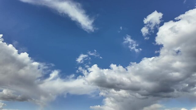 Time-lapse, low angle view, of a blue sky with evolving white color cottony cumulus clouds