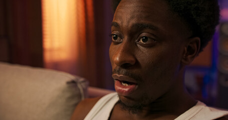 A young male figure sits on the couch wearing a comfortable sleeveless shirt, watching television...