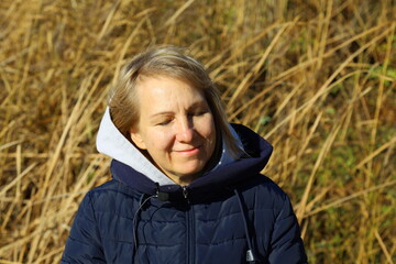 Woman in warm jacket enjoying a peaceful moment amidst golden autumn grass under the gentle embrace of sunlight on a crisp day