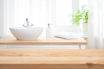 Empty wooden table top as mock up for product montage on blurred bathroom sink interior  background