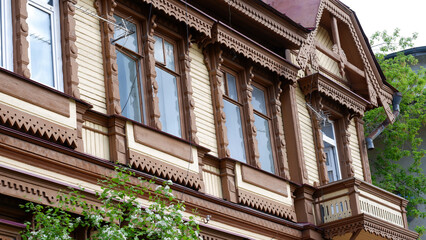 Vintage brown wooden building in a modern city. Traditional Russian architecture, wooden windows with carved frames.