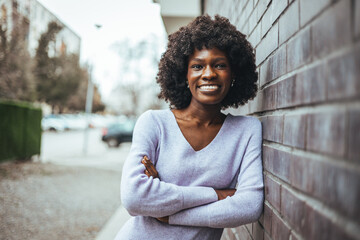 Confident Woman Smiling Outdoors While Leaning Against a Brick Wall
