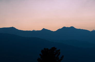 Dusky sky above serene mountain silhouettes, fading light casting peaceful hues across the quiet, forested landscape.