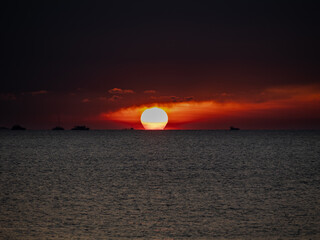 Fiery sunset over the ocean with silhouetted boats, taken at Sunset Village Beach Resort,...