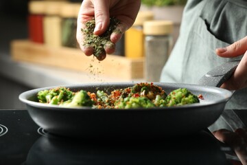 Woman adding spices to dish in kitchen, closeup