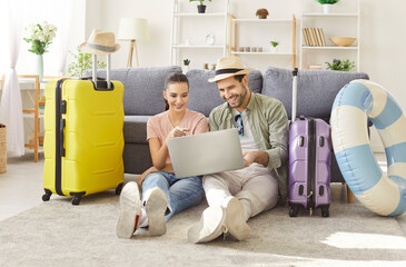 Happy newlywed couple online booking flight tickets, tourists suitcases packed, wheel luggage in...