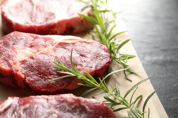 Pieces of raw beef meat and rosemary on black table, closeup