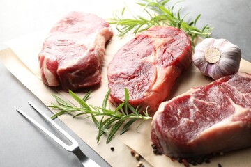 Pieces of raw beef meat, spices and carving fork on grey table, closeup