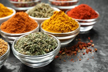 Different aromatic spices in bowls on dark table, closeup