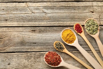 Different aromatic spices in spoons on wooden table, flat lay. Space for text