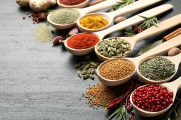Different aromatic spices in spoons on black table, closeup. Space for text