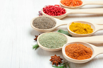 Different aromatic spices in spoons on white wooden table, closeup