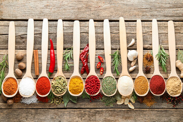 Different aromatic spices in spoons on wooden table, flat lay