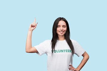 A young woman wearing a volunteer t-shirt smiles confidently while raising her finger, portraying...