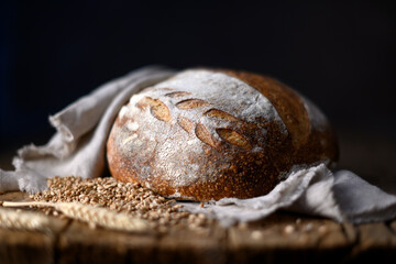 Crusty leavened sourdough bread with a rough browned skin on aged wooden surface wrapped in a linen towel . Homemade wild yeast loaf styled for rustic kitchen photography