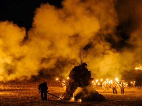 Night scene of a bonfire with figures holding torches. Smoke fills the air, illuminated by the firelight. Krampus and St Nicholas, 5 December in Tarvisio, Friuli Venezia Giulia, Julian Alps, Italy.