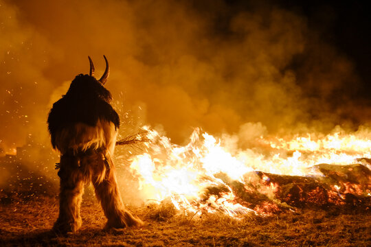 A Krampus figure stands before a large bonfire, smoke fills the air. Krampus and St Nicholas, 5 December in Tarvisio, Friuli Venezia Giulia, Julian Alps, Italy.