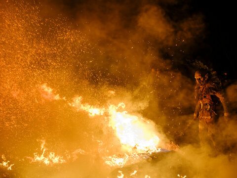 A Krampus figure stands amidst a fiery display, sparks flying in the dark. The figure is dressed in a traditional costume with a grotesque mask. Krampus and St Nicholas, 5 December in Tarvisio, Italy