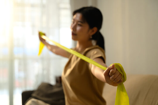 Asian woman using resistance band for arm exercises in a bright living room