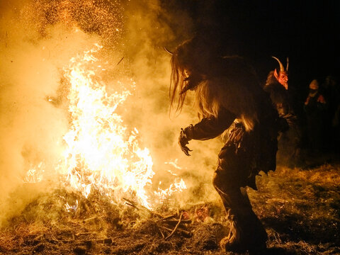 Silhouette of a Krampus figure tending a large bonfire, sparks flying. Krampus and St Nicholas, 5 December in Tarvisio, Friuli Venezia Giulia, Julian Alps, Italy.