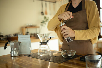 Young woman grinding coffee beans by hand in a kitchen preparing for fresh pour over brew