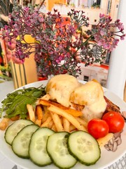 a plate with French fries, meat with cheese, tomatoes, cucumbers cut into pieces, spicy herbs and artificial flowers in a vase.Food background