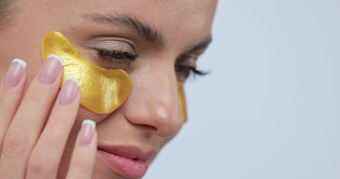 Close-up of beautiful smiling woman in gold eye patches smiling over gray background. Beauty care and cosmetic products for facial skincare.