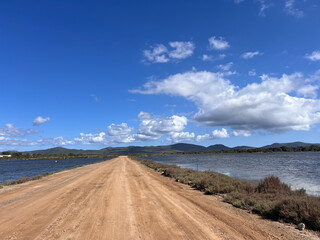 Strada sterrata che passa attraverso una laguna a Cagliari e che punta verso le montagne e un cielo azzurro con poche nuvole