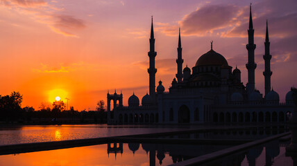 Obraz premium Silhouette of a mosque at sunset with a bright sun on the horizon and an orange-colored sky above it