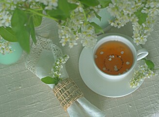 Cup of tea on the table with spring fresh bouquet with white blooming fragrant branches of bird cherry.