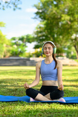Fototapeta premium fit woman doing yoga and listening to music on headphones in the park