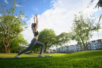 Young woman practicing yoga in a warrior pose on a mat in a sunny park