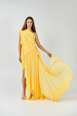 Beautiful woman in flowing yellow dress showcases summer fashion in a bright, airy studio setting