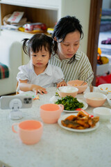 Mother and daughter enjoy meal together while watching something on mobile device at home during daytime