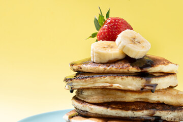 Pancakes with chocolate and fruit on yellow background. Copy space