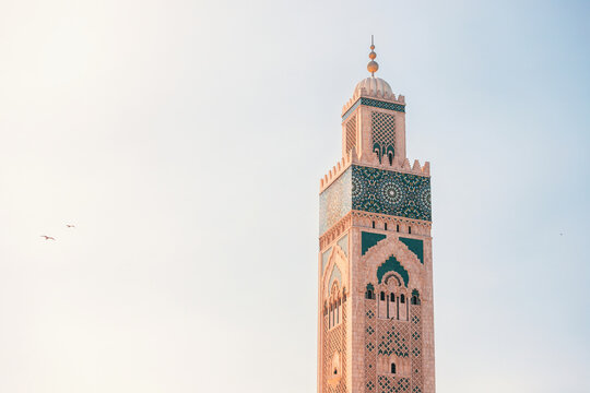 Sunlight illuminating the intricate details of the Hassan II Mosque minaret against a clear sky, showcasing Moroccan architecture