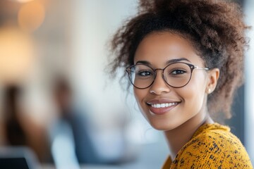 Portrait of a smiling woman with glasses and curly hair in a bright office setting looking at camera
