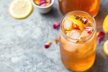 Refreshing Iced Tea with Citrus and Floral Garnish in Glass on Rustic Surface.