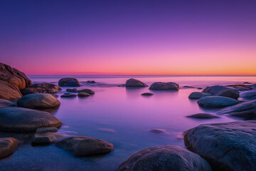  Dreamy long exposure of a rocky seascape bathed in golden and purple sunset light, creating a peaceful and atmospheric coastal scene