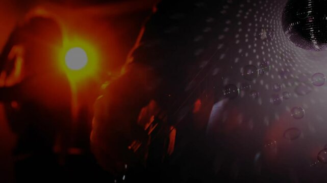 Band performing on stage, guitar swinging under red light, disco ball spinning, bubbles drifting