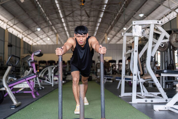 Fototapeta premium Pushing Limits: Young Man Training with Weighted Sled at Gym