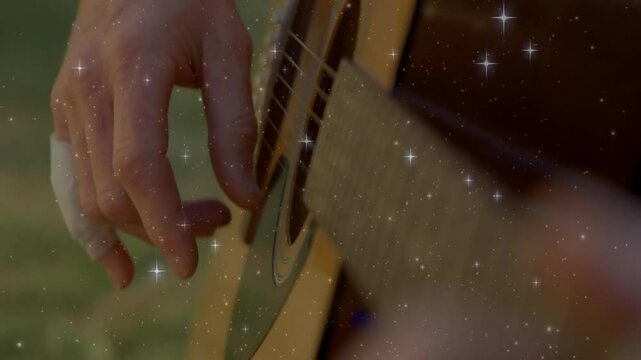 Guitarist hand pressing guitar strings in music studio corner, with star-like animated specks