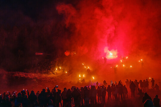 A crowd watches figures with torches through red smoke. Krampus and St Nicholas, 5 December in Camporosso Valcanale, Tarvisio, Italy.