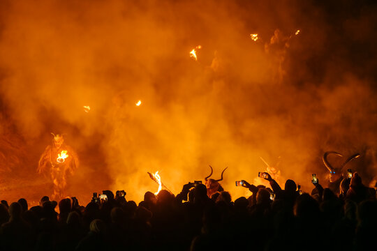 Silhouetted crowd watches Krampus figures with torches emerge from smoke and fire. Krampus and St Nicholas, 5 December in Camporosso Valcanale, Tarvisio, Italy.