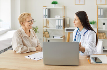 Portrait of a young female doctor talking with sick mature smiling woman patient during...